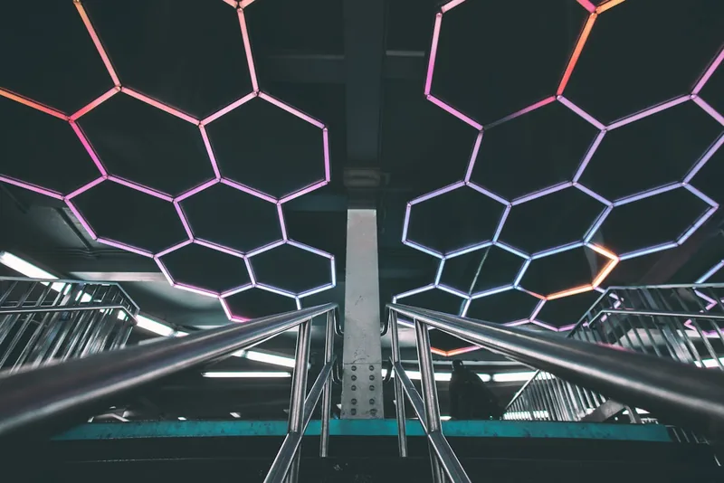 Futuristischer Raum mit Rolltreppen und farbig beleuchteter geometrischer Decke.