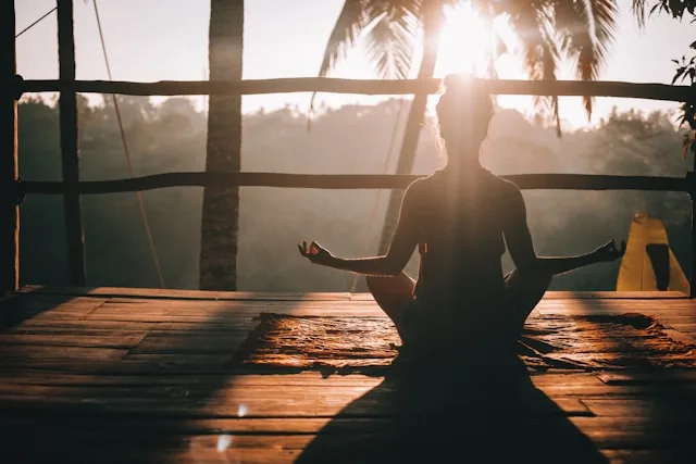 Person im Meditationssitz auf einer Holzterrasse im Sonnenlicht.